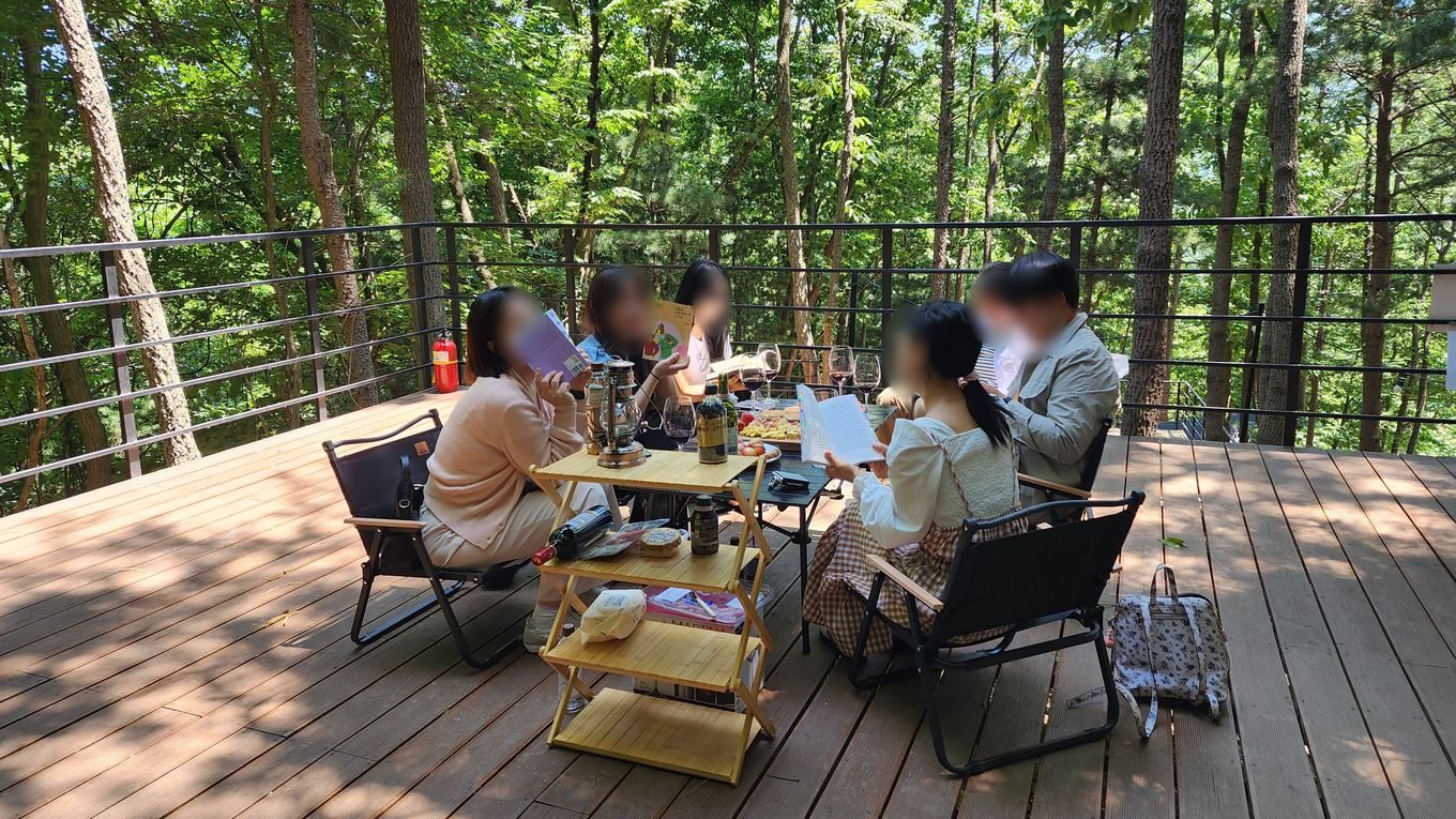 숲속 데크에 둘러앉아 각자 가져온 책을 읽는 주말 트립 참가자들
